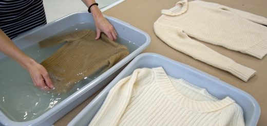 Hands gently stretching a shrunken wool sweater on a flat surface, illustrating the process of unshrinking clothing.