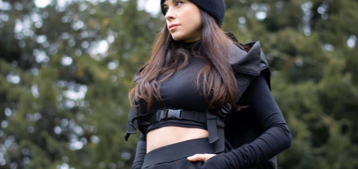A woman stands in a city wearing a blush pink cropped techwear jacket with high-waisted jeans